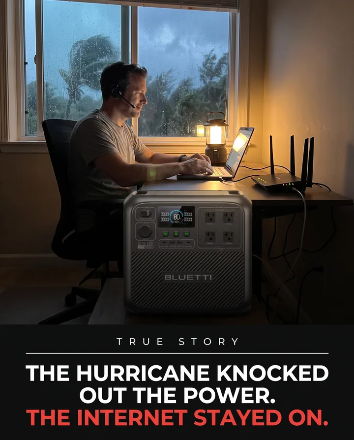 Spec ad for BLUETTI. A man works on a laptop by lantern light during a hurricane with an Elite 200 V2 at his desk, under the headline: The hurricane knocked out the power. The internet stayed on.